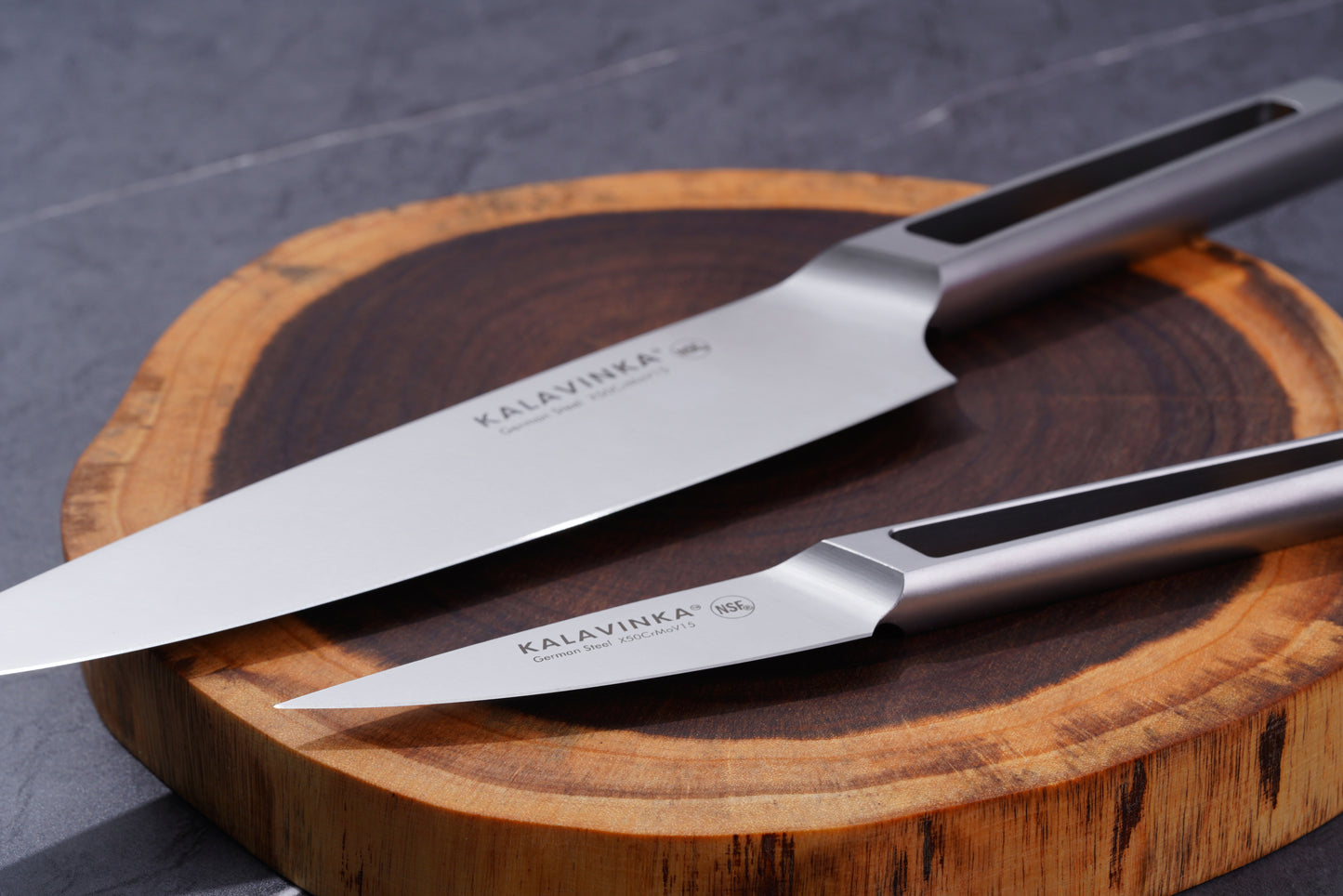 A close-up image features two knives from the VENDANA Series 2-Piece Essentials Knife Set, an 8-inch chef's knife and a 3.5-inch paring knife, both elegantly placed on a wooden cutting board. These high-carbon stainless steel knives by KALAVINKA showcase sleek, modern designs with ergonomic, black-striped handles.