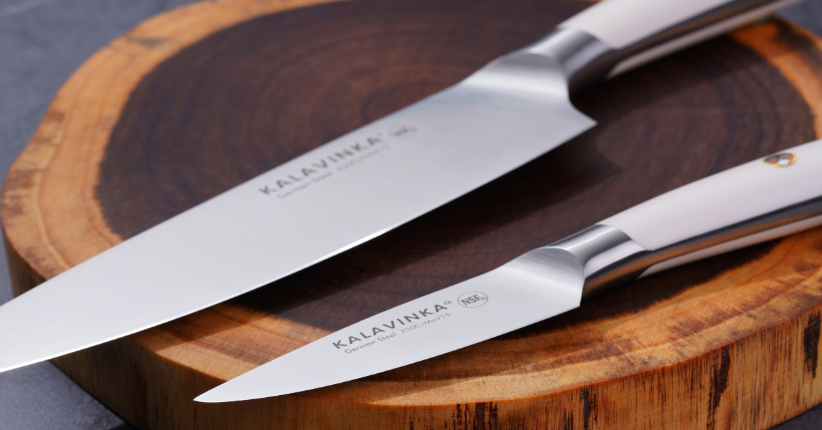 A close-up showcases two knives from the KALAVINKA SAMJNA Series. The larger one, a 7-Inch Santoku knife, rests elegantly on a round wooden cutting board alongside its counterpart featuring a narrow, pointed tip. Both knives display sleek metallic finishes and are crafted from corrosion-resistant German X50CrMov15 steel, complete with ergonomic handles for enhanced comfort.